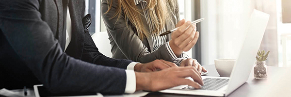 Hombre y mujer de negocios sentados en un escritorio, trabajando uno al lado del otro mientras miran una computadora portátil.